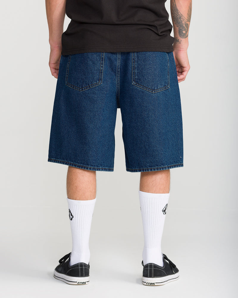 Rear view of a person wearing Volcom Men’s Billow Denim Short 22 in indigo, white crew socks, and black sneakers.