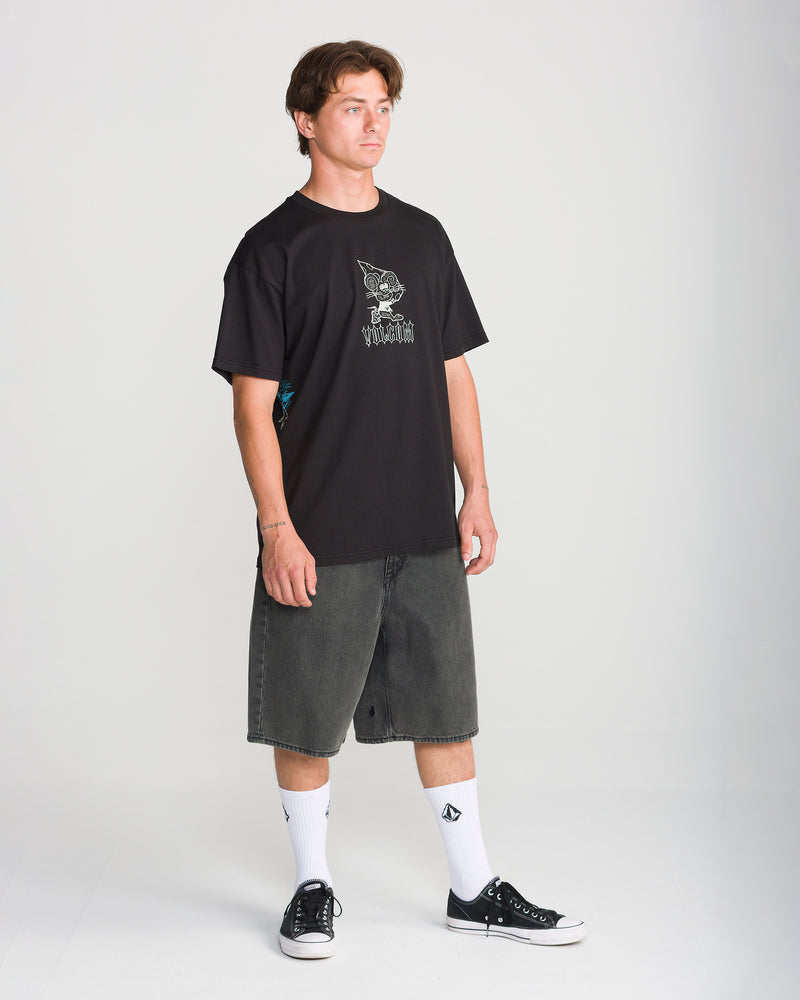 A person wearing a black graphic t-shirt, loose-fit Men’s Billow Denim Short 22 by Volcom, white crew socks, and black sneakers.