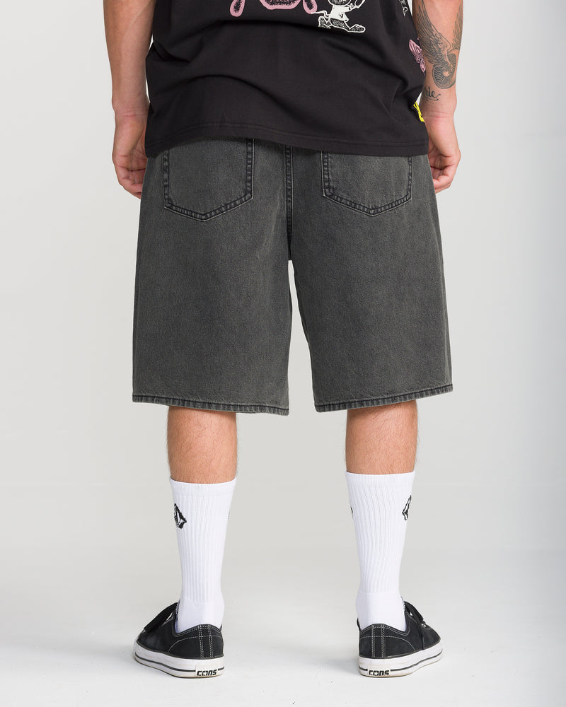 Back view of Volcom Men’s Billow Denim Short 22 loose-fit black denim shorts ending at the knee, worn with white crew socks and black sneakers.