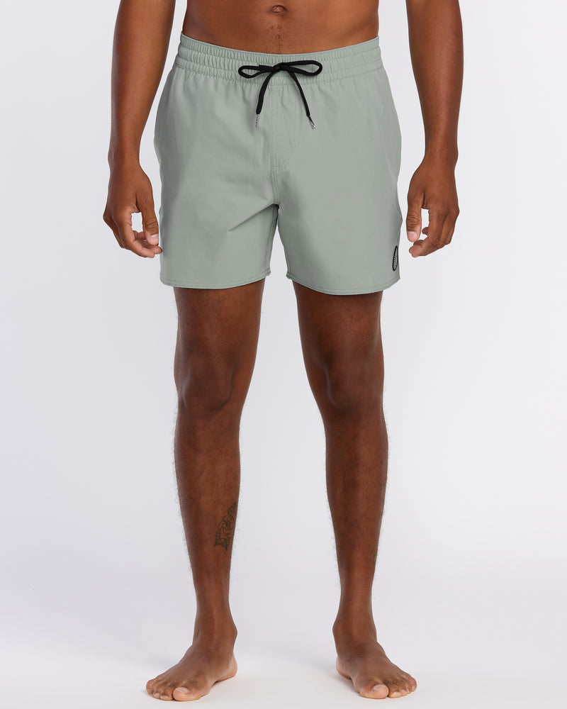 A person stands barefoot in Volcom Men's Lido Solid 16" Trunks, light gray with a black drawstring and small logo on the left leg. The 2-way stretch swim trunks are cropped at the torso; background is plain white.