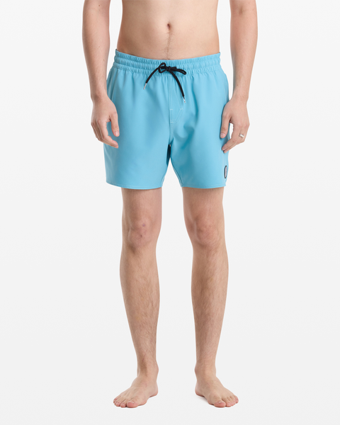 A man stands barefoot against a white background, wearing Volcom Men's Lido Solid Trunk 16 swim trunks in light blue with a black drawstring and small round logo on the left leg. His upper body is not visible.