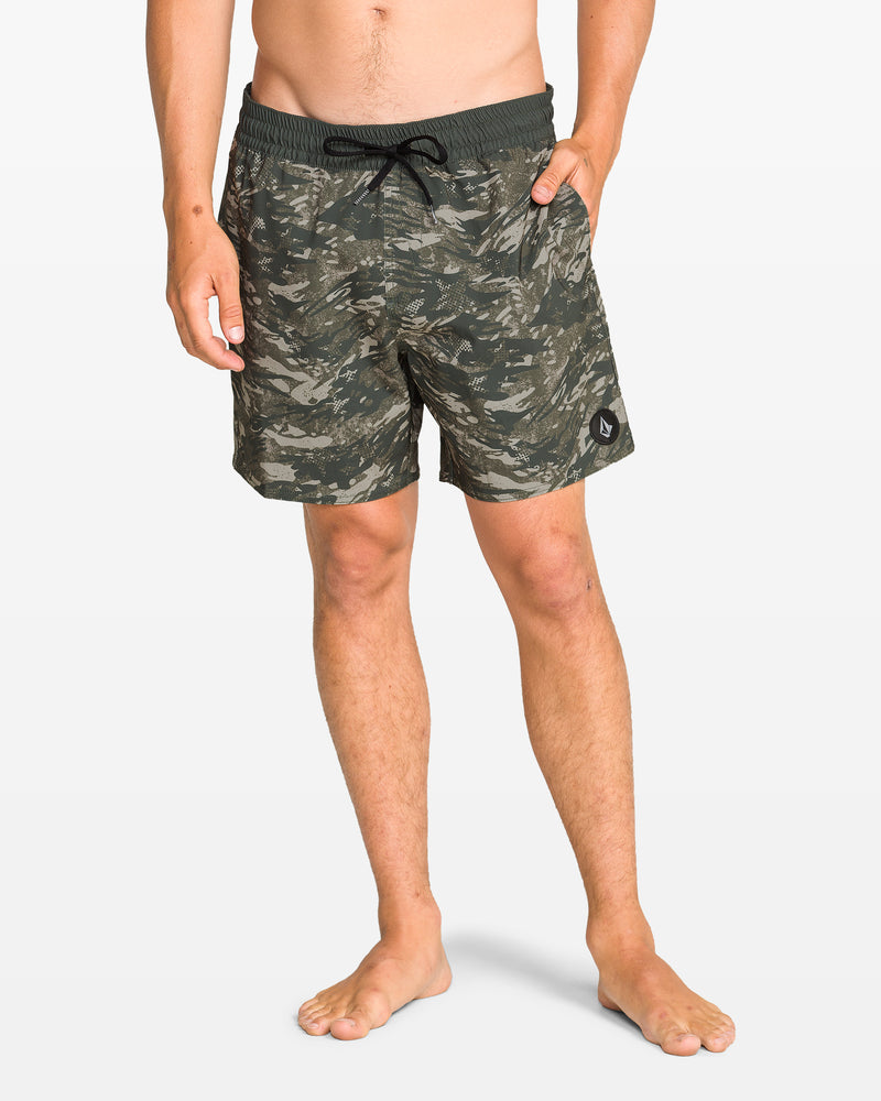A person stands barefoot against a plain white background, wearing Volcom Men's Lido Print Trunks in a green camo pattern with a black drawstring and 4-way stretch fabric, hands in pockets.