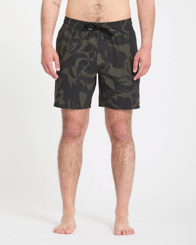 A person stands barefoot against a white background, wearing Volcom Men's Psyche Cotton Trunk 17 swim shorts with a dark green and black camouflage pattern, elastic waistband, and drawstring. The image is cropped from shoulders down.