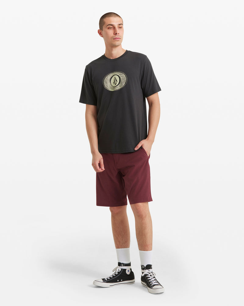 A young man showcases classic Volcom style in a black graphic tee, white socks, black high-top sneakers, and maroon Men's Frickin Cross Shred Static Shorts by Volcom against a white background, one hand casually in his pocket as he looks to the side.