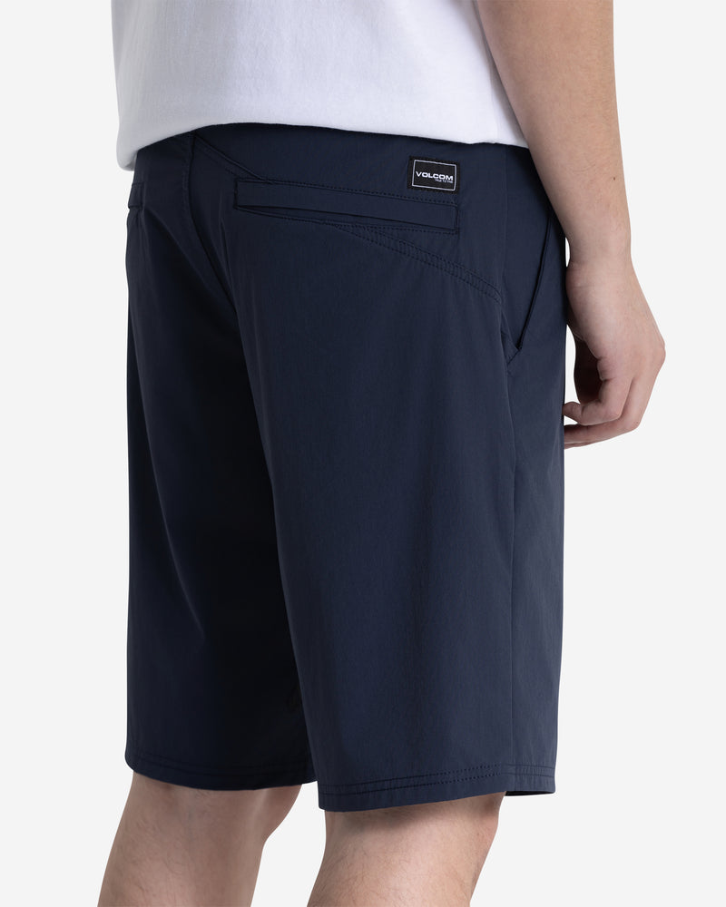 A person in a white shirt and Volcom Men's Frickin Cross Shred Shorts (navy, 20" outseam) is shown from the side and back, with their right hand resting by their side.
