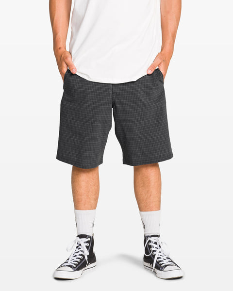 A person stands with hands in pockets, wearing a white T-shirt and Volcom Men's Mix Frickin Cross Shred Shorts with a recycled buckle button, paired with white crew socks and black Converse sneakers. Photo cropped from chest down on a white background.