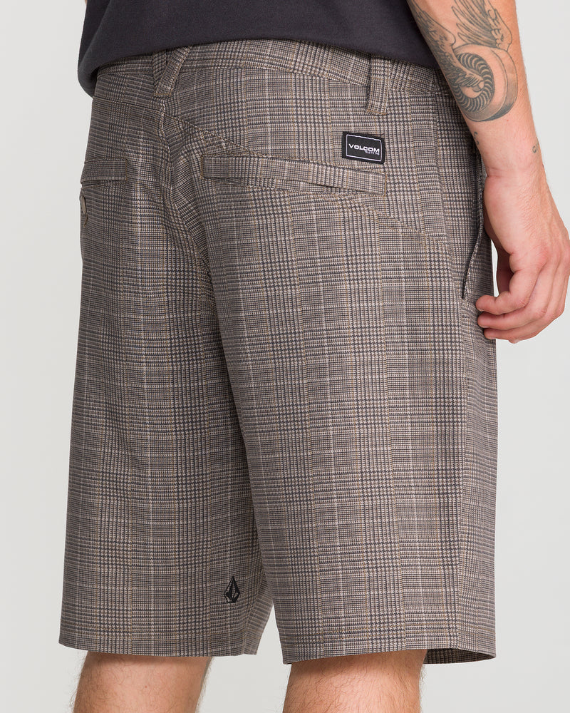 A person wearing Volcom Men’s Mix Frickin Cross Shred 20 modern-fit shorts with pockets, featuring a visible brand label and a tattoo on their arm, stands against a plain light background.