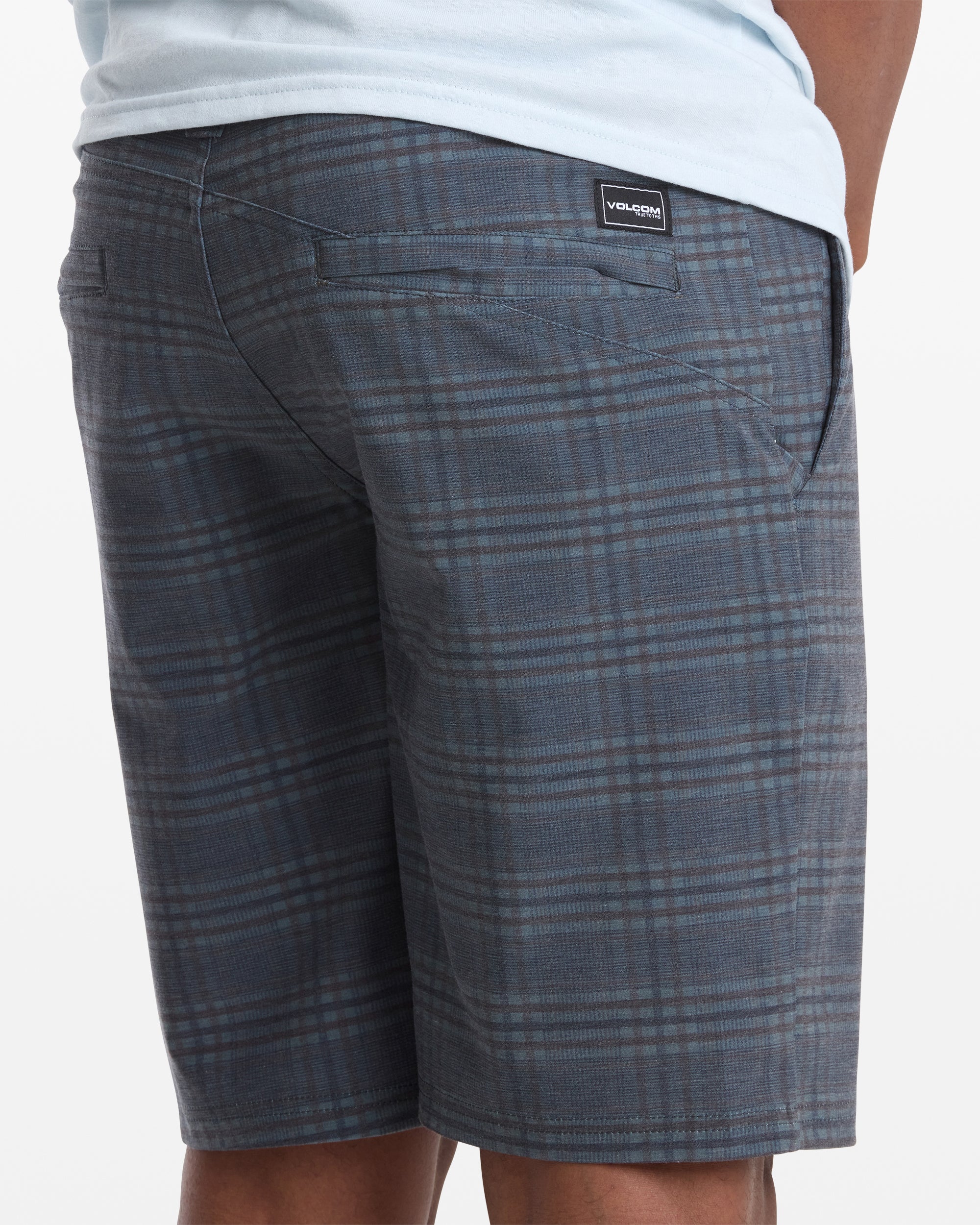 A person wearing Volcom Men's Mix Frickin Cross Shred Shorts in blue-gray plaid and a light blue shirt is seen from the back, with the Volcom label above the right pocket.