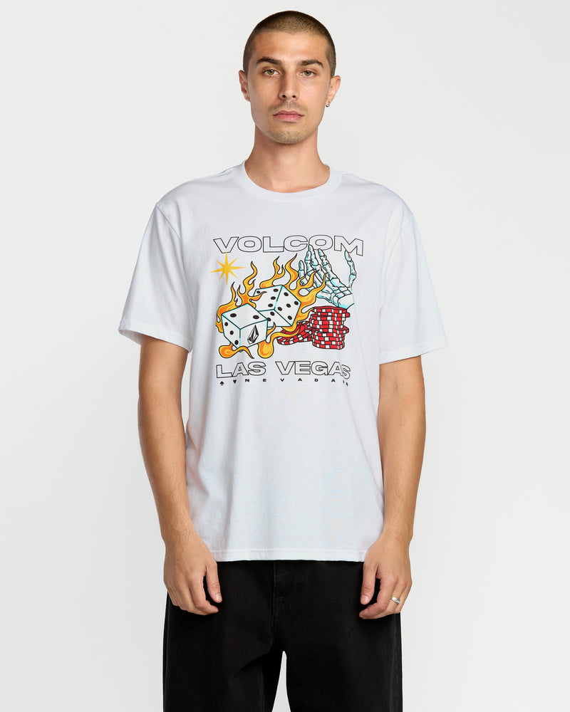 A man with short hair wears the Volcom Men's Pass Line Short Sleeve Tee, a white graphic T-shirt featuring flaming dice, playing cards, and poker chips with Las Vegas Nevada text, crafted from premium ring-spun cotton.