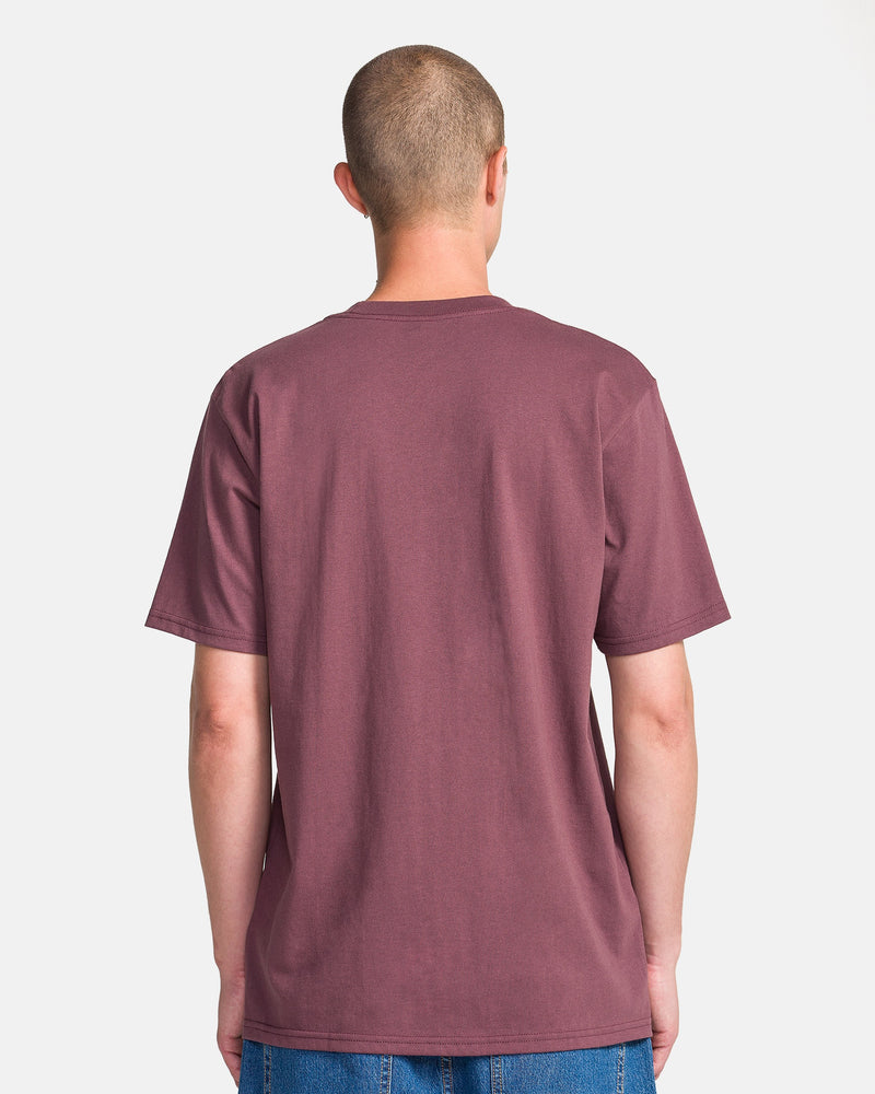 A person with short hair stands with their back to the camera, wearing a plain maroon Men's Yoink Short Sleeve Tee by Volcom and blue jeans against a light background.