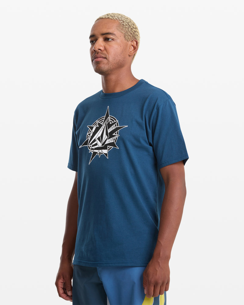A man with short blond hair wears the Volcom Men's Yoink Short Sleeve Tee, 100% cotton with a white geometric graphic, paired with blue athletic shorts featuring a yellow stripe, standing against a plain white background.