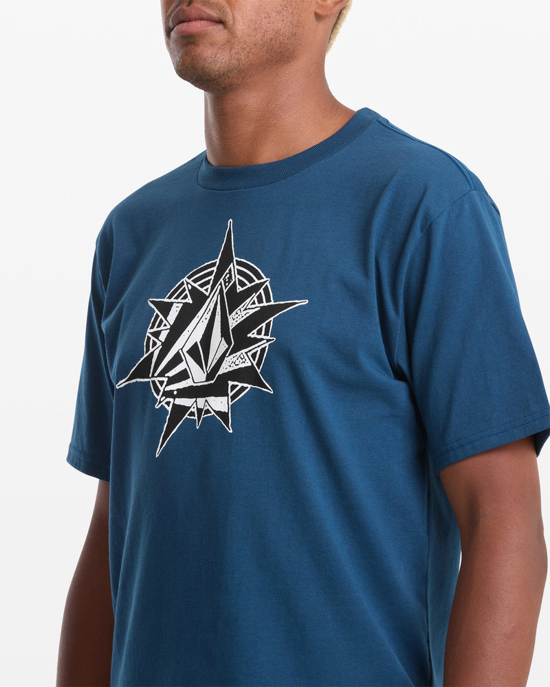 A man wears the Volcom Men's Yoink Short Sleeve Tee, featuring a blue classic fit and bold black and white geometric soft-hand screen print on the chest, standing against a plain white background.