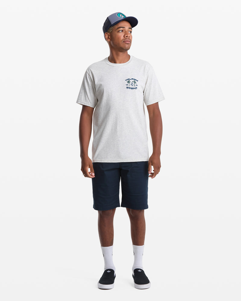 A man poses against a white background wearing the Volcom Men's Fed Up Short Sleeve Tee in gray, featuring a soft-hand screen print on the chest, paired with navy shorts, white socks, black sneakers, and a navy baseball cap.