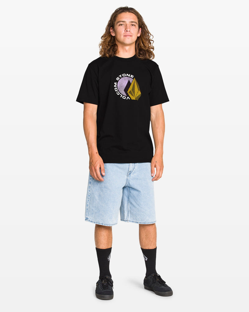 A person with long, wavy hair wears a black Volcom T-shirt, light blue knee-length denim shorts, black socks with a white logo, and black sneakers, standing against a white background.
