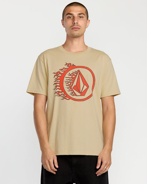 A man stands against a plain white background wearing the Volcom Men's Circle Stone Short Sleeve Tee, a classic fit crew neck made from premium ring spun cotton with a red geometric logo surrounded by flames on the front.