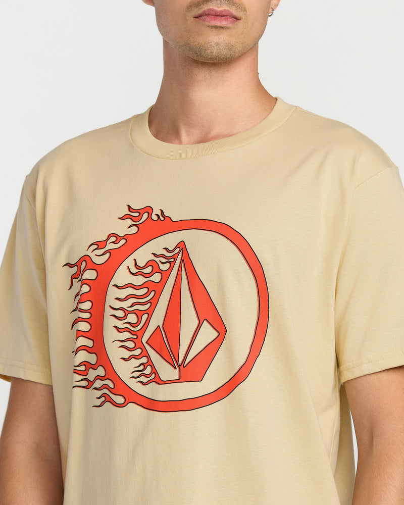 A person wears the Volcom Men's Circle Stone Short Sleeve Tee, a classic fit crew neck in premium ring spun cotton, featuring a large red geometric flame design inside a circle on the front. The head and crew neck are partially out of frame.