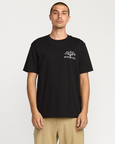 A man faces forward wearing the Volcom Men's Always Ripping Short Sleeve Tee in black, featuring a classic fit and soft-hand screen printed Volcom branding on the left chest, paired with beige pants, set against a plain white background.