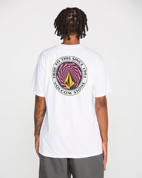 A person with short braids wears the Volcom Men's Dirty Work Short Sleeve Tee—a classic fit, white heavyweight cotton t-shirt featuring a large, colorful Volcom Stone logo and the text “TRUE TO THIS SINCE 1991 VOLCOM STONE” in soft-hand screen print on the back. The person is standing with their back to the camera.
