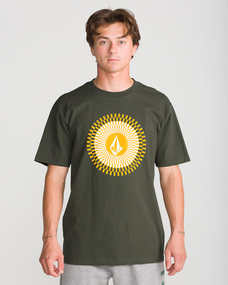 A young man stands facing forward against a plain light background, wearing the Volcom Men’s Radiate Short Sleeve Tee in dark green, featuring a yellow and white geometric sunburst design.