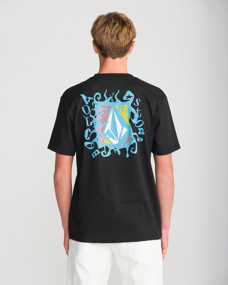 A person viewed from behind wearing a black Volcom Men’s Framer Short Sleeve Tee, featuring a colorful, abstract graphic print on the back with a central stone-shaped emblem.