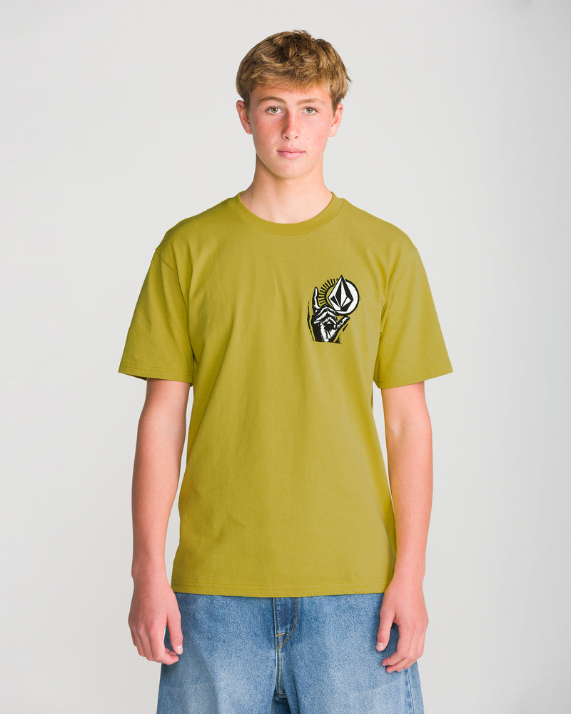 A teenage boy stands against a plain background, wearing the Volcom Men’s Opposition Short Sleeve Tee in greenish-yellow with a black-and-white chest logo, paired with loose blue denim shorts.