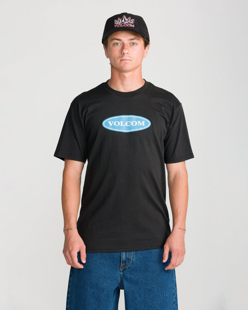 A man wearing a black Volcom Men’s Remastered Stone Short Sleeve Tee with a blue archival logo on the chest and a black baseball cap.