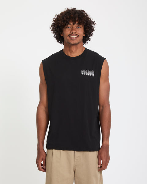 A man with curly hair, wearing Volcom’s Men's Gamma Doom Sleeveless black shirt with a small white chest graphic and beige pants, stands facing the camera against a plain white background.