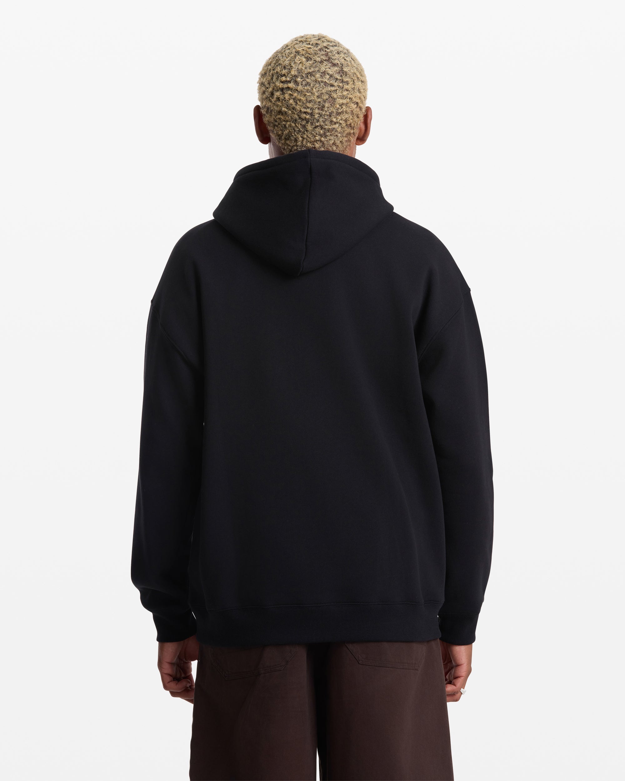 A person with short, light-blond hair faces away from the camera, wearing a black Men's Volcom Stone Pullover fleece hoodie by Volcom and dark pants, set against a plain white background.