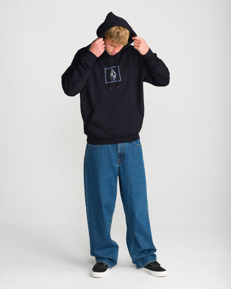A person stands against a plain white background, adjusting the hood of the black Volcom Men’s Quadratic Pullover with a geometric design, styled with blue baggy jeans and black sneakers. Brushed-back fleece ensures added comfort.