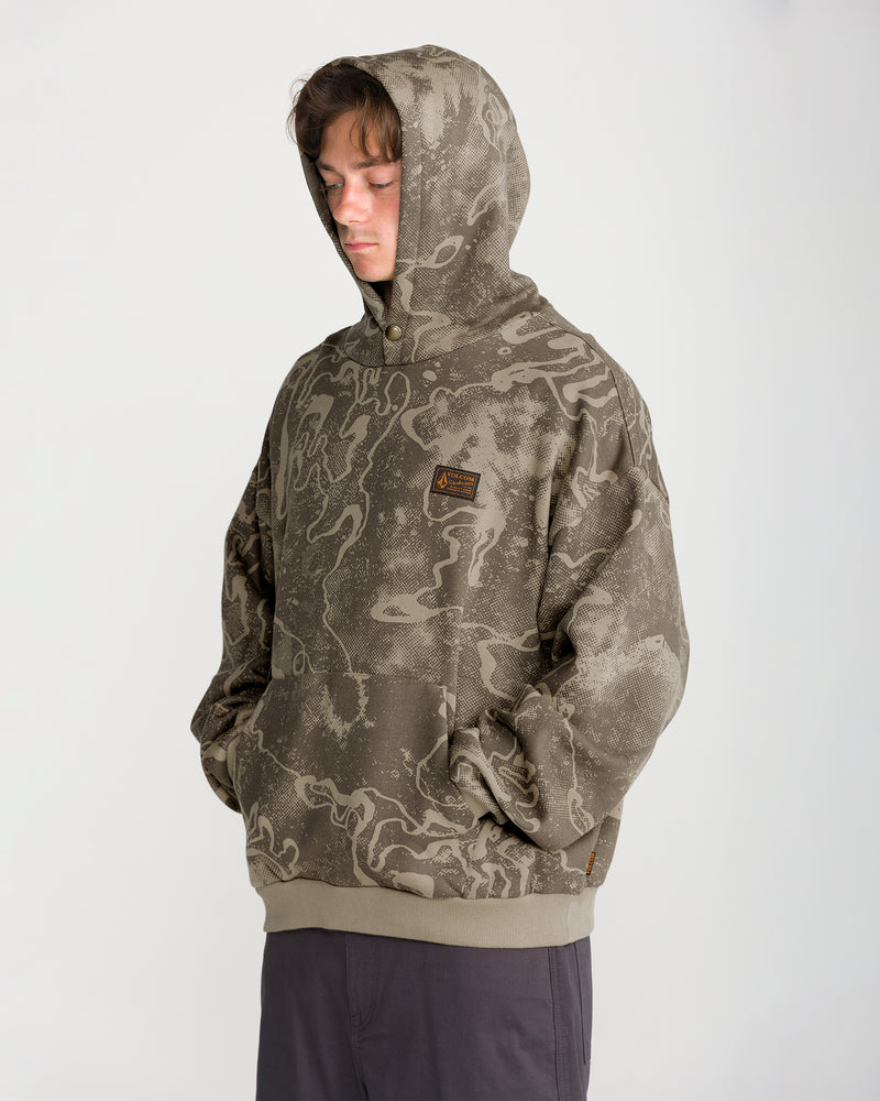 A person wearing a Volcom Men’s Hailstorm Workwear Pullover in olive green with a dark abstract camouflage print and a rectangular chest patch.