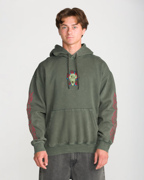 A man wears a Volcom Men’s Featured Artist Casey Jones Pullover, an olive green hoodie with a screaming head graphic in flames on the chest and red flame designs down the sleeves.