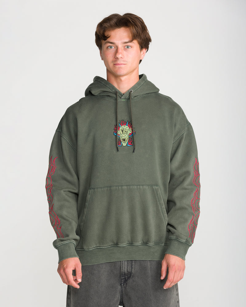 A man wears a Volcom Men’s Featured Artist Casey Jones Pullover, an olive green hoodie with a screaming head graphic in flames on the chest and red flame designs down the sleeves.