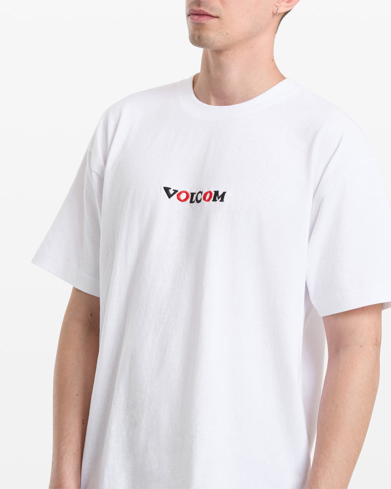A person wears the Volcom Men's Featured Artist Seth Conboy Loose Short Sleeve Tee, featuring a plain white design with "VOLCOM" in black and red text on the chest, standing against a white background.
