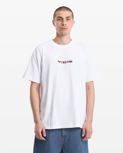 A man with short hair wears the Volcom Men's Featured Artist Seth Conboy Loose Short Sleeve Tee and blue denim shorts, standing against a plain white background.