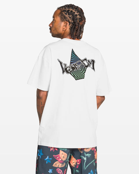 A person faces away, wearing the Volcom Men's Sea Legs Short Sleeve Tee in white with a large abstract graphic and logo on the back, paired with colorful butterfly-print shorts. The background is plain white.