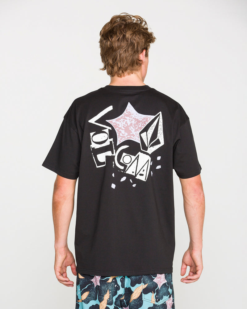 A person with short, light brown hair is seen from behind wearing the Volcom Men's Concrete Jungle Short Sleeve Tee in black—crafted from heavyweight ringspun cotton and showcasing bold graphic designs along with "Volcom" printed on the back. They are also sporting vibrant, patterned shorts.