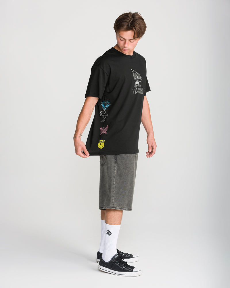 A person wears a black Volcom Men’s Featured Artist Casey Jones Short Sleeve Tee with colorful illustrations, paired with grey shorts and black sneakers.