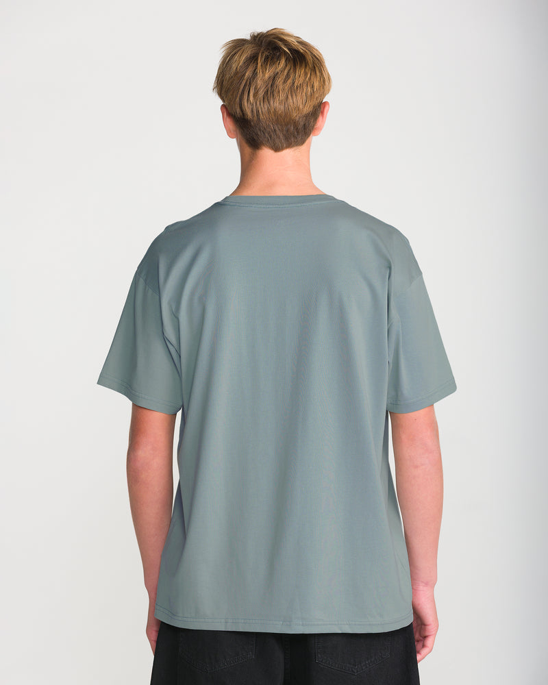 Back view of a person wearing a grey, heavyweight Men’s Hand Held Short Sleeve Tee with a loose fit and black pants.