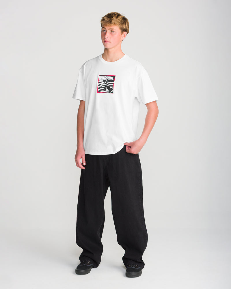 A person wearing a Volcom Men’s Hand Held Short Sleeve Tee, a loose fit cotton t-shirt with a chest graphic, paired with black pants and sneakers.