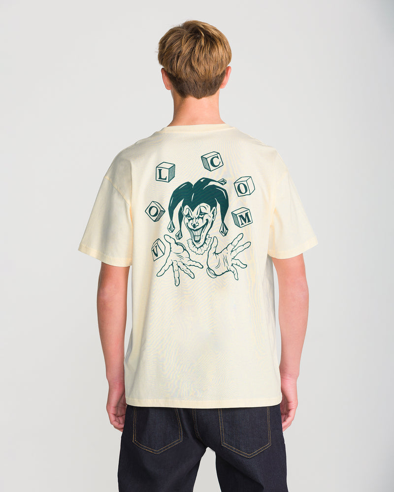 A person seen from behind wears an off-white, loose fit Men’s Last Laugh Short Sleeve Tee featuring a graphic of a jester surrounded by floating blocks that spell VOLCOM.