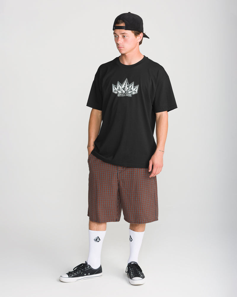A person wearing a black Men’s Tooms Short Sleeve Tee with a graphic on the chest, brown and black plaid shorts, white crew socks, and black sneakers.