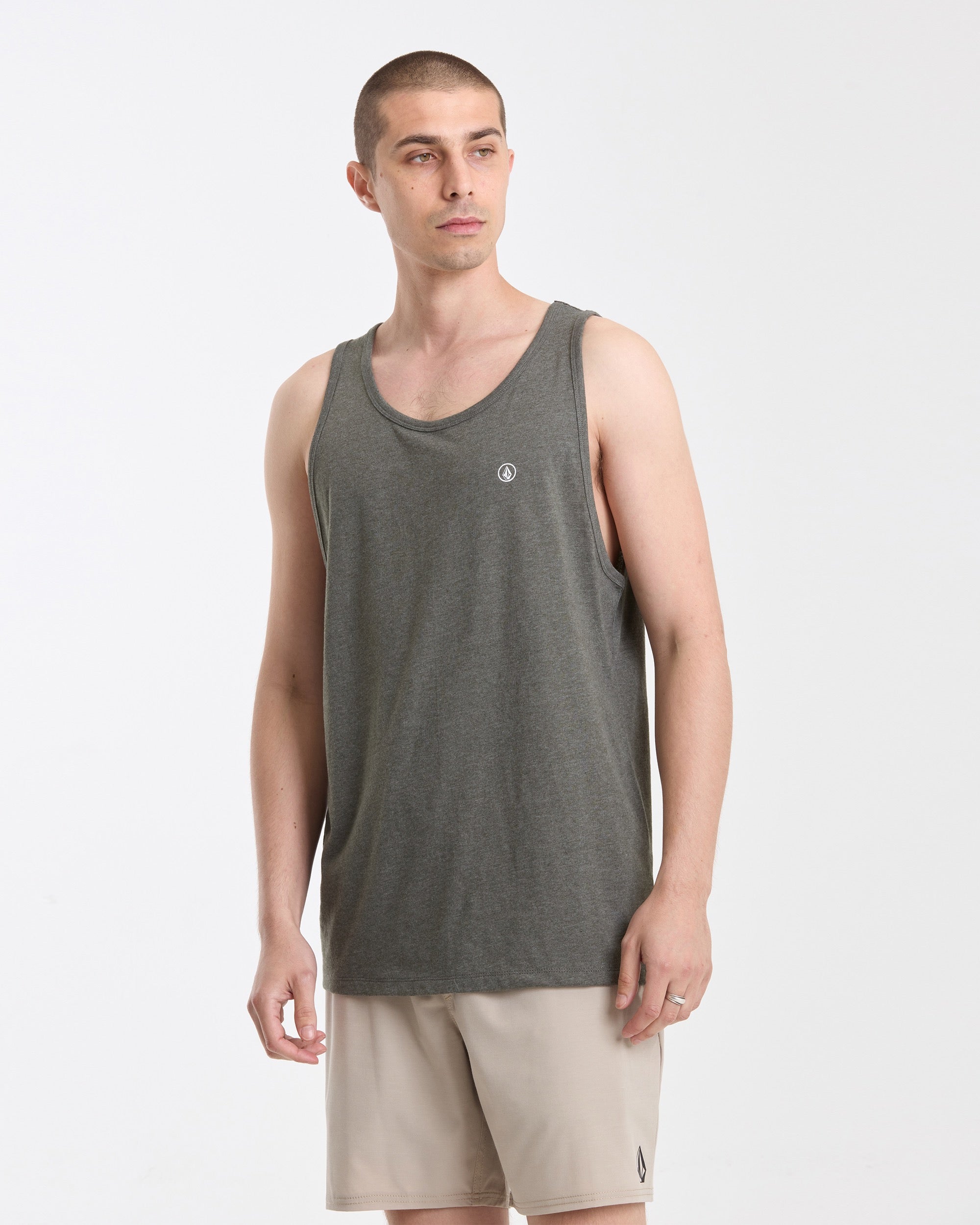 A man in a gray Men's Solid Heather Tank by Volcom and light beige shorts stands against a white background, gazing off to the side with a neutral expression.