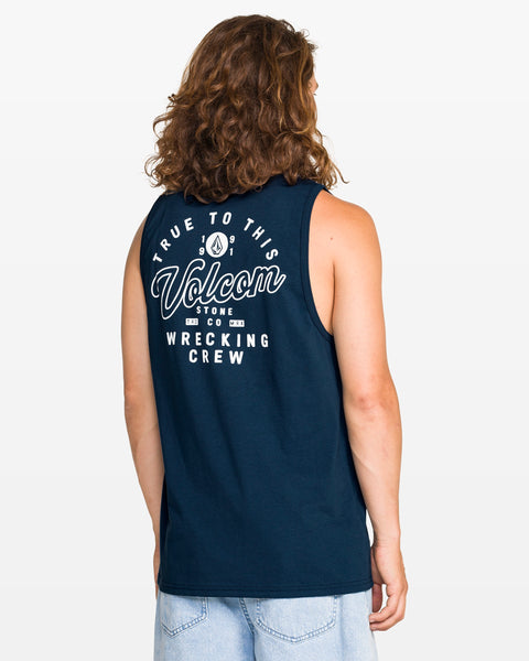 A person with long hair, seen from the back, wears a navy blue Volcom Men's Wrecking Tank in classic fit with "True To This, Volcom Stone Co, Wrecking Crew" printed in white on the back, paired with light blue jeans.