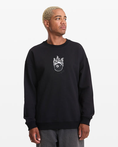 A person with short blonde hair models the Volcom Men's Featured Artist Seth Conboy Crew, a black fleece crewneck with small flaming yin-yang embroidery on the chest, standing against a plain white background and looking to the side.