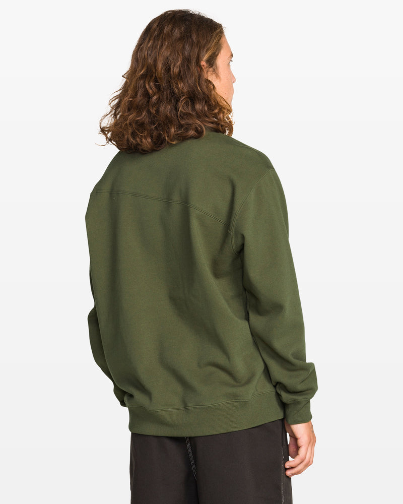 A person with shoulder-length wavy brown hair wears the Volcom Men's Stone Cruiser Crew in Squadron Green—made from recycled polyester—and black pants, facing away from the camera against a plain white background.