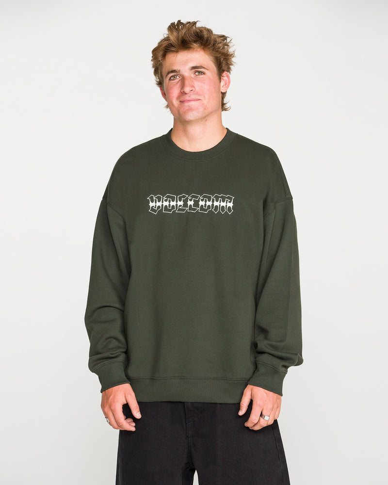 A person with short, tousled hair wears the Volcom Men's Dirty Work Crew— a green, loose fit fleece crew sweatshirt crafted from recycled polyester—paired with black pants and standing against a plain light background. The sweatshirt features white text for added style and offers both comfort and sustainability.