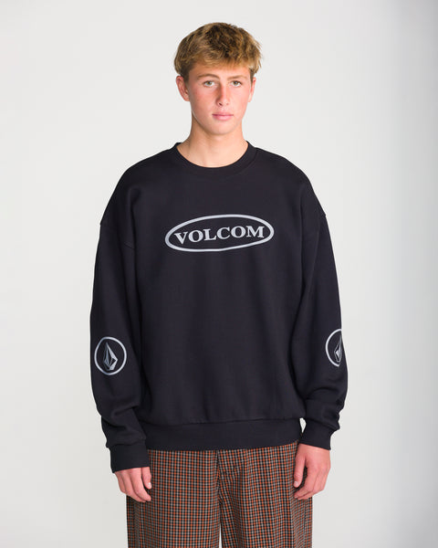 A person wearing a black Volcom Men’s Stone Op Crew sweatshirt featuring a grey oval graphic on the chest and circular logos on each sleeve.