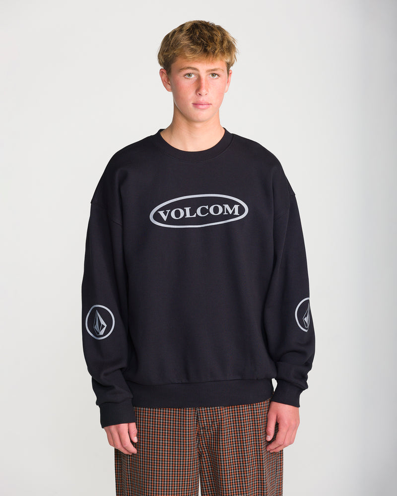 A person wearing a black Volcom Men’s Stone Op Crew sweatshirt featuring a grey oval graphic on the chest and circular logos on each sleeve.