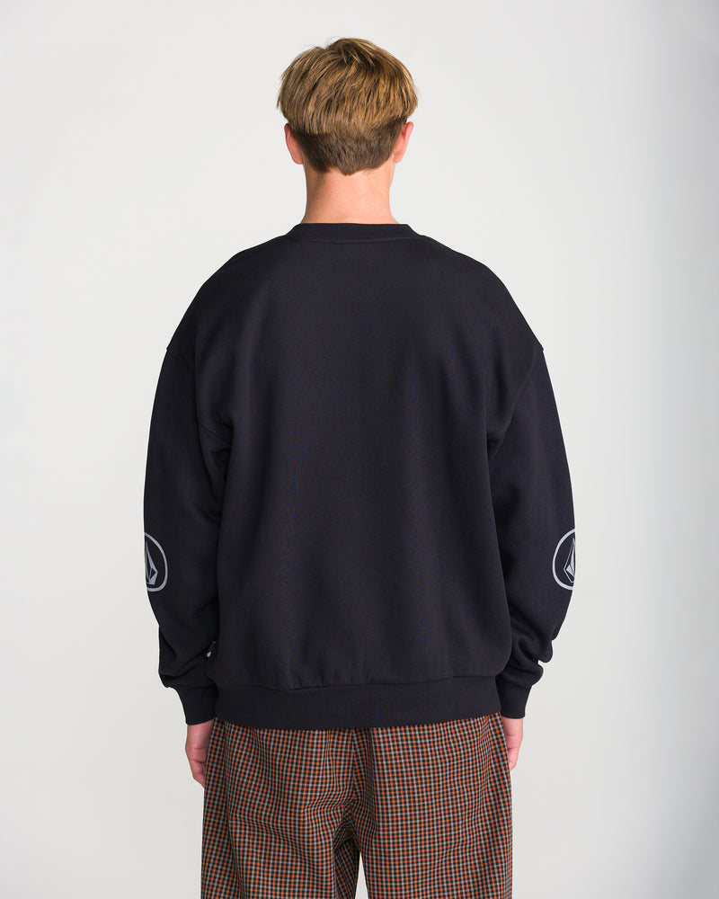 Back view of a person wearing a loose-fit, black Men’s Stone Op Crew sweatshirt with a Volcom graphic logo on each sleeve.