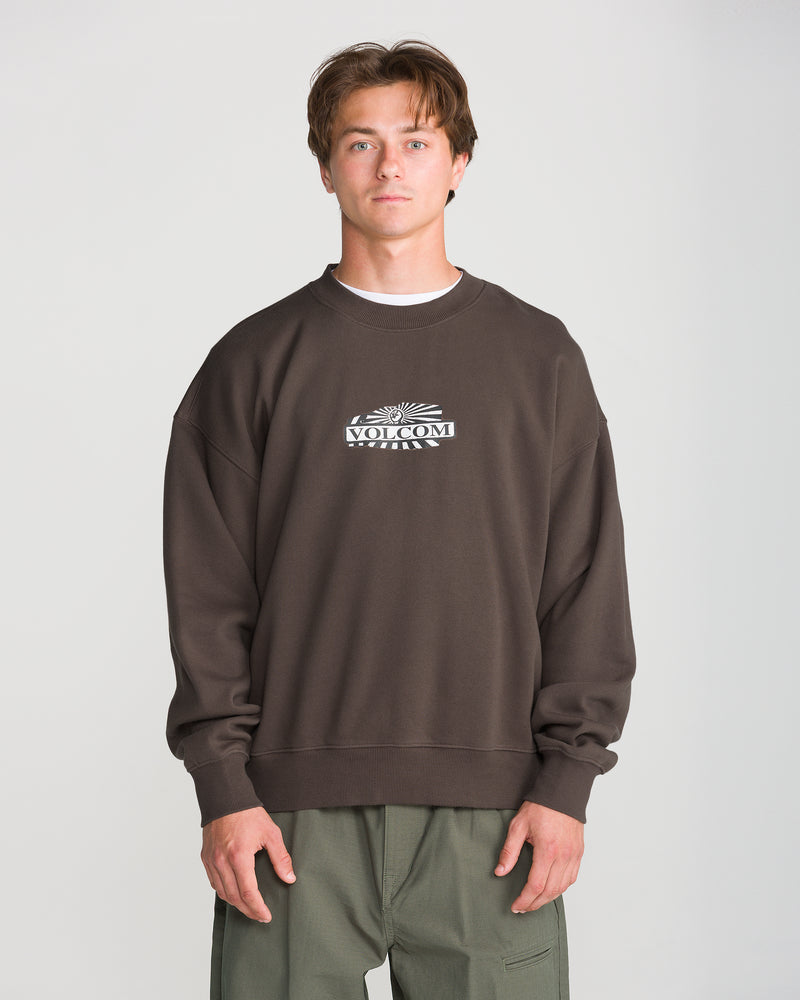 A person wearing a dark brown, vintage wash Men’s Stone Op Crew sweatshirt featuring a VOLCOM graphic on the chest.